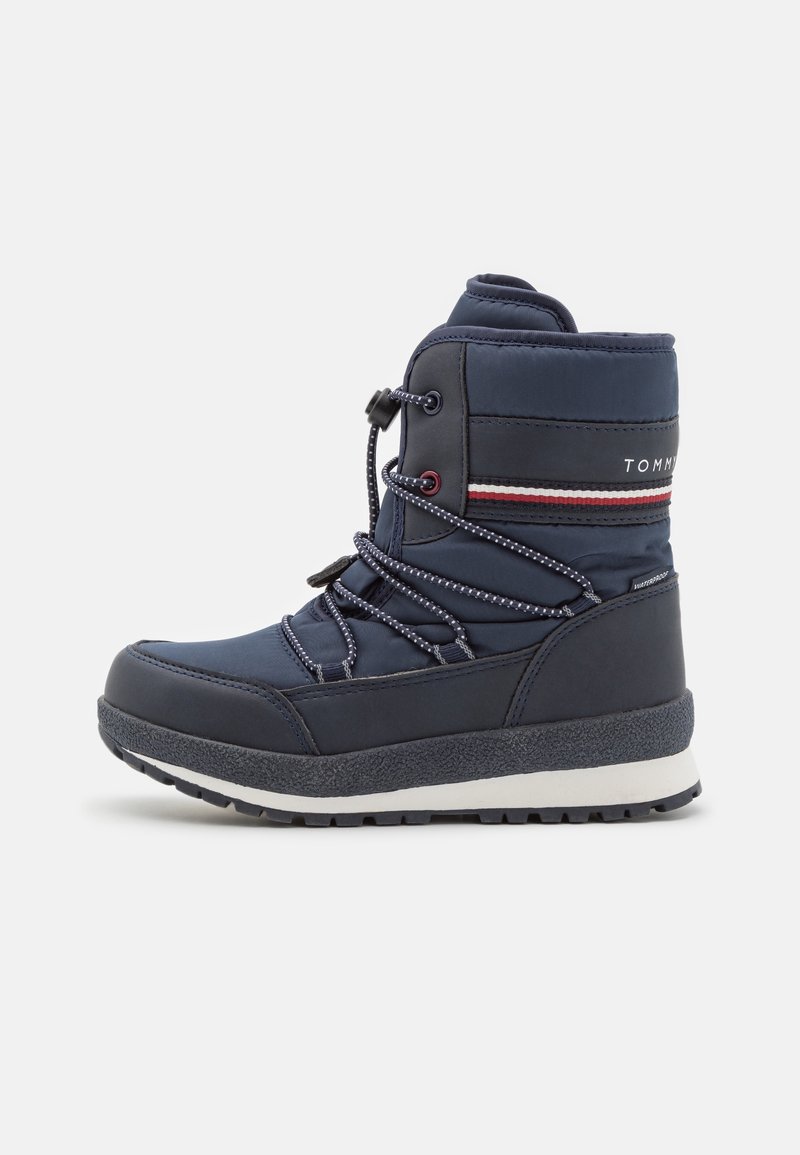 Botte d'hiver isolée bleu marine avec bande blanche et rouge, semelle noire et lacets élastiques ajustables sur fond blanc.