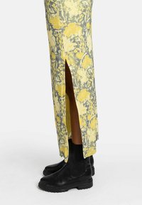 Gonna maxi floreale in tessuto giallo e grigio, con alte fessure laterali. Indossata con stivaletti neri alla caviglia. Texture liscia, design leggero.