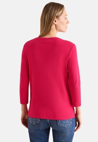 Getailleerde top met driekwart mouwen in felroze katoen. Heeft een ronde halslijn en een iets verlengde achterkant. Gepaard met blauwe denim jeans.