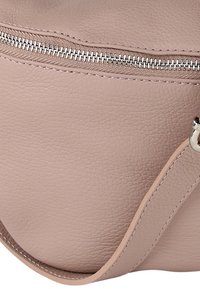 Lichtroze leren tas met een textuur, voorzien van een zilveren ritssluiting en een brede riem met gestikte accenten.