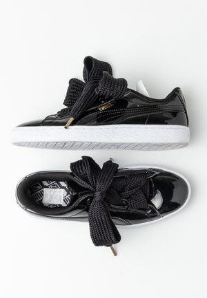 Sorte blanke sneakers med tykke sorte snørebånd bundet i sløjfer, hvide såler og guld Puma-logo på siden, vist fra top- og sidevinkler.