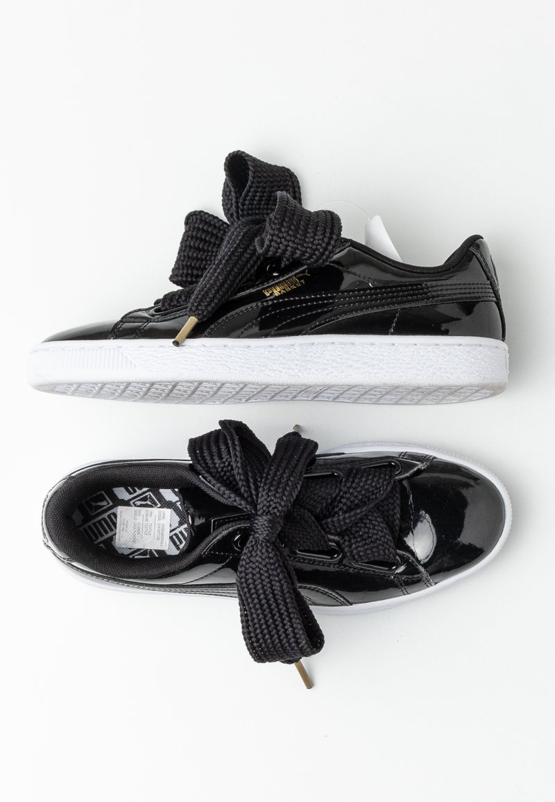 Baskets noires brillantes avec de grosses lacets noirs noués en nœuds, semelles blanches et logo Puma doré sur le côté, vues de dessus et de profil.