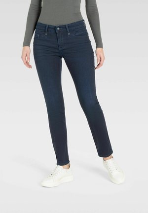Dunkelblaue Skinny Jeans aus Denim mit einer glatten Textur. Verfügt über ein klassisches Fünf-Taschen-Design und Gürtelschlaufen. Getragen mit weißen Sneakers.
