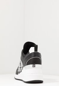 Sneaker noir et blanc avec un motif tissé texturé, des accents en cuir lisse, une cheville rembourrée et une semelle en caoutchouc avec un talon rehaussé.