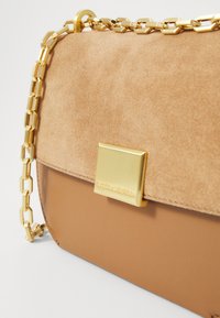 Borsa a spalla in suede beige e pelle liscia con tracolla in catena dorata e chiusura metallica che presenta un dettaglio del logo.