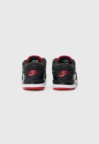 Baskets Nike noires avec des accents rouges, présentant une tige en cuir lisse, un col rembourré et une semelle extérieure blanche avec des détails rouges.