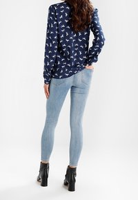 Námořnická blůza s koňským vzorem, dlouhými rukávy, v kombinaci s světle modrými přiléhavými džíny a černými kotníkovými botami. Hladká tkanina, přesný střih, minimální detaily.