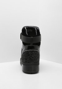 Černé vysoké tenisky s třpytivou patou, suchým zipem a logem Michael Kors na podrážce, zobrazené ze zadní strany na bílé ploše.