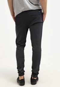 Tmavě námořnické teplákové kalhoty s zužujícím se střihem, elastickými manžetami a dvěma zadními kapsami. Tkanina je hladká s mírným leskem.