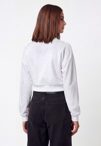 Sudadera blanca corta con mangas largas y dobladillo acanalado, combinada con vaqueros negros de talle alto con bolsillos traseros. Textura suave, diseño minimalista.