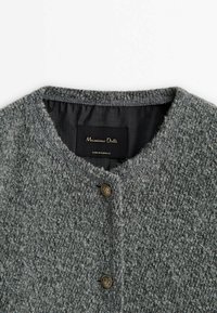 Cardigan gris texturé avec un col rond, comportant deux boutons dorés et une doublure intérieure noire. Étiquette "Massimo Dutti" visible.