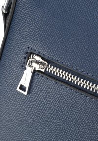 Primo piano di una zip in metallo argentato su un materiale in pelle blu scuro texture, parte di una borsa o portafoglio.
