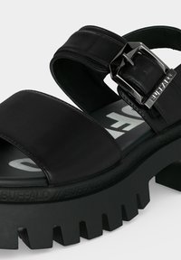 Χοντρό μαύρο πλατφόρμε σανδάλι με φαρδιές λουρίδες, μεγάλο ασημένιο αγκράφα και βαθιά σόλα με ανάγλυφο λογότυπο Buffalo.