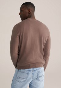 Pull à manches longues marron avec un col rond, des poignets et un ourlet inférieur côtelés, associé à un jean en denim bleu clair. Texture douce, sans motifs.
