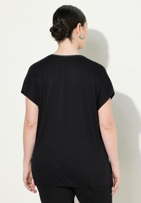 Top nero a maniche corte con vestibilità ampia, scollatura rotonda e orlo elasticizzato. Tessuto liscio con una leggera lucentezza, che mostra un design semplice.