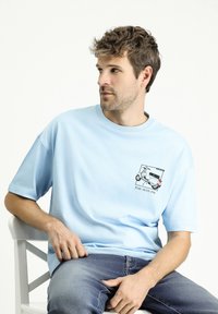 Camiseta de algodón azul claro con mangas cortas, que presenta una impresión gráfica de un vehículo y el texto "Conduce conmigo" en el área del lado izquierdo del pecho.