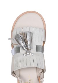 Infradito in pelle beige chiaro con design a frange, dettagli in argento e nappine metalliche decorative. Texture liscia con punta arrotondata.