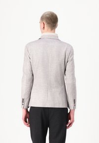 Blazer ajusté gris clair avec une texture subtile, revers cranté et quatre boutons aux poignets, vu de dos.