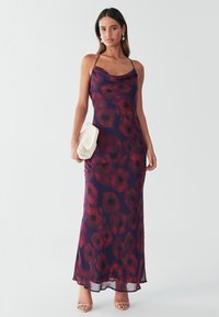 Dlouhé, bezrukávové šaty z průsvitné fialové látky s květinovým vzorem v červené barvě s černými středy. Kombinováno s krémově zbarveným psaníčkem.