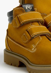 Stivali in suede giallo con doppie fibbie in Velcro, cuciture bianche a contrasto e un accento nero sul tallone. Sole in gomma spesso con battistrada.