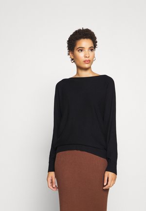 Black knitted sweater with a wide neckline and long sleeves, featuring a ribbed hem. Worn over a brown ribbed skirt.