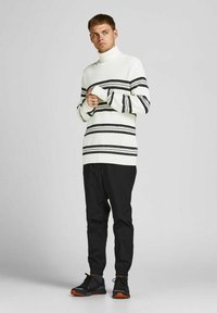 Weiß gestreifte Rollkragensweater mit schwarzen horizontalen Streifen, kombiniert mit schwarzen tapered Hosen und schwarzen Sneakers mit orangefarbenen Akzenten.