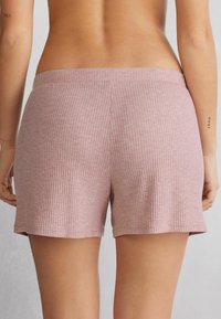 Hladké bavlněné šortky v světlé růžové barvě, s širokým pasem a volnějším střihem. Šortky mají jemnou texturu bez viditelných švů.