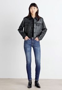 Μαύρο δερμάτινο μπουφάν με κουμπιά μπροστά, δύο τσέπες στο στήθος, γιακά, συνδυασμένο με εφαρμοστά μπλε τζιν παντελόνια και μαύρες μπότες μέχρι τον αστράγαλο.