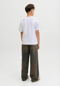 Bijela pamučna majica i široke maslinasto zelene hlače, prikazane odostraga. Hlače imaju izblijedjeli izgled i vidljive džepove.