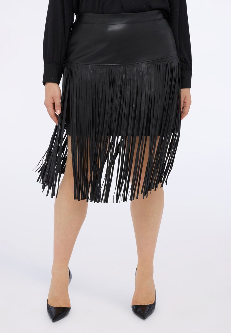 Czarna skórzana spódnica z frędzlami o dopasowanej talii i teksturowanym wykończeniu; asymetryczne frędzle sięgają poniżej linii dołu, w zestawieniu z czarnymi, spiczastymi obcasami.