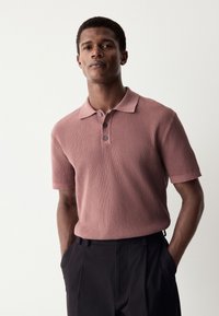 Polo met korte mouwen in geribbelde textuur, poederroze kleur, met een kraag en een drieknopensluiting. Broek niet gedetailleerd.