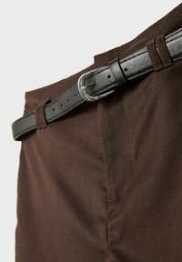Primo piano di pantaloni marroni fissati con una cintura in pelle nera sottile con una fibbia argentata.