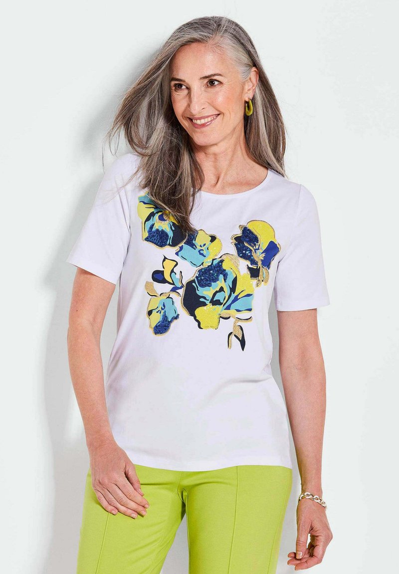 Weißes T-Shirt mit kurzen Ärmeln, das ein florales Design in Blau und Gelb aufweist. Der Stoff ist glatt, mit einem runden Ausschnitt und einem lockeren Schnitt.