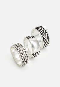 Trois bagues en argent : l'une avec un design en maillons de chaîne, l'une lisse et l'une avec un motif en chevrons. Largeurs et textures variées.