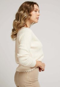 Pull léger en crème fabriqué dans un matériau doux, avec des poignets et un ourlet côtelés à bord ondulé, associé à un pantalon ajusté beige clair.