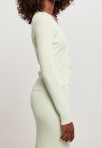 Světle zelený žebrovaný cardigan s dlouhými rukávy, přiléhavý design a zapínání na knoflíky. Měkká textura a hladký povrch.