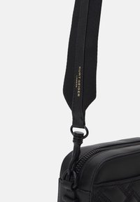 Borsa a tracolla in pelle nera con un design trapuntato, zip resistente, tracolla regolabile in tessuto testurizzato e dettaglio di branding in oro.