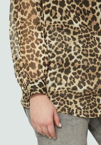 Leopardenmuster Bluse aus einem transparenten, strukturierten Stoff. Mit Puffärmeln und einem gerafften Bündchen. Farbpalette umfasst Beige- und Brauntöne.