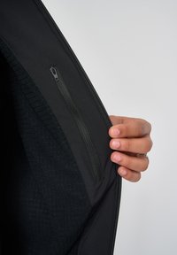 Schwarze Jacke mit einem Innenfutter aus strukturiertem Stoff. Verfügt über eine mit Reißverschluss verschlossene Tasche auf der linken Seite und eine glatte Außenseite.