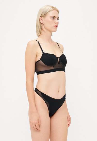 Black lingerie set featuring a padded bralette with sheer mesh panels and adjustable straps, paired with a high-cut thong.