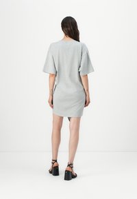 Gray cotton t-shirt dress with short sleeves, casual fit, and a rounded hem. Worn with black heeled sandals. Plain texture, minimal design.