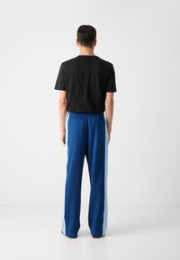 Pantalones deportivos azules con paneles laterales en azul claro, cinturilla elástica y diseño de pierna recta, combinados con una camiseta negra.