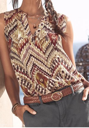 Vícebarevný top bez rukávů s geometrickým vzorem v červených, zlatých a hnědých tónech; doplněný o pletený hnědý pásek a tmavé kalhoty.