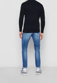 Marinblå stickad tröja med ett texturerat randigt mönster, kombinerad med ljusblå smala jeans och grå sportskor med vita inslag.