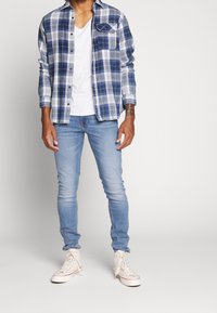 Blå och vit rutiga flanellskjorta, vit V-ringad t-shirt, ljusblå skinny jeans och vita högklackade sneakers. Snygg passform, avslappnad design.