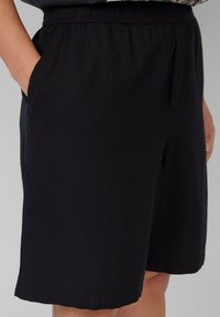 Zwarte, knielange shorts van zacht materiaal met een elastische tailleband en zijzakken. Eenvoudig ontwerp zonder zichtbare patronen of versieringen.