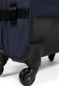 Valigia blu navy con base nera texture, dotata di ruote lisce e cinghie. Il design enfatizza la durabilità e la mobilità.