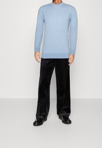Pull en tricot à manches longues bleu clair avec un col côtelé, associé à un pantalon large noir et des chaussures en cuir verni noir.