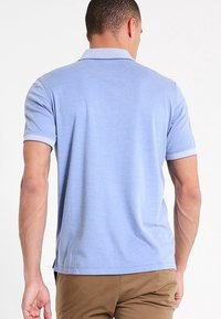 Polo à manches courtes bleu clair avec une texture douce. Il présente un col et des poignets contrastants avec une bordure subtile, ainsi qu'un ourlet arrondi.