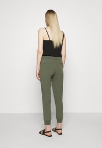 Calças verde-oliva com um design afunilado, punhos elásticos e bolsos traseiros, combinadas com um top preto sem mangas e sandálias.